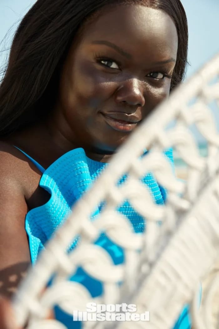 Nyma Tang poses in a vibrant blue bikini behind a white chair.